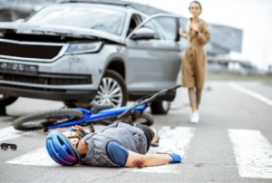 Cyclist lying injured on the crosswalk next to a car while a woman stands nearby